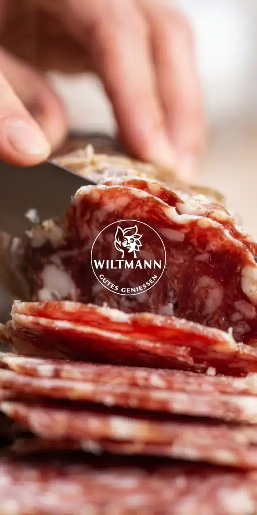 Hand schneidet Salami in Scheiben – Link zur Referenz Wiltmann